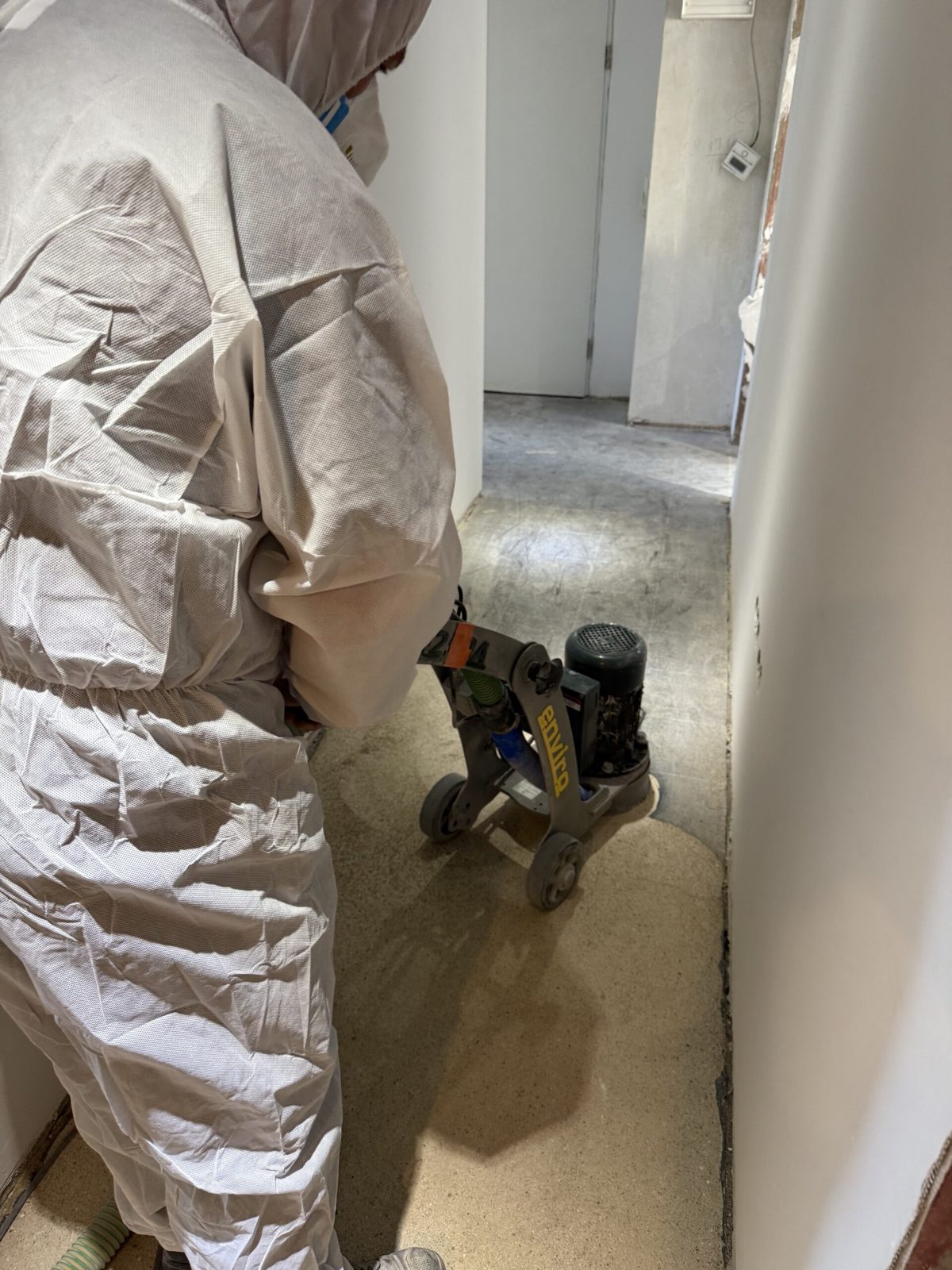 Fachkraft in Schutzanzug beim staubarmen Abschleifen eines asbesthaltigen Bodenklebers